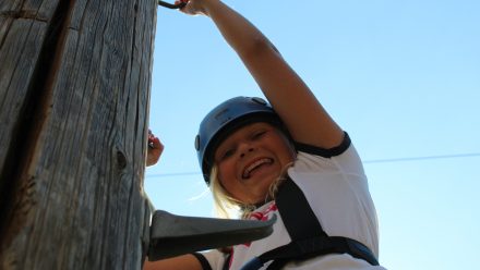 young girl climbing a pole smiling down at camera